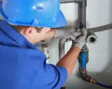 Instalator montuje odpowietrzenie kanału sanitarnego w domu parterowym, łącząc rury.