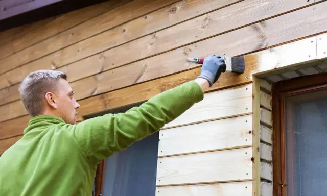 Mężczyzna maluje deskę elewacyjną, tworząc piękne aranżacje. Drewno nabiera nowego blasku.