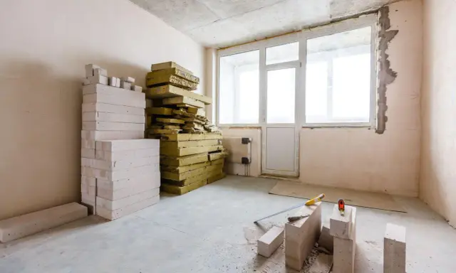 Materiały budowlane: pustaki i wełna mineralna, gotowe do ocieplenia od wewnątrz. Narzędzia budowlane leżą na podłodze.