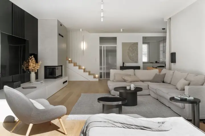 Nowoczesny salon z szarą sofą, kominkiem i schodami. Pokazuje, jakie są style wnętrz, łącząc minimalizm z przytulnością.