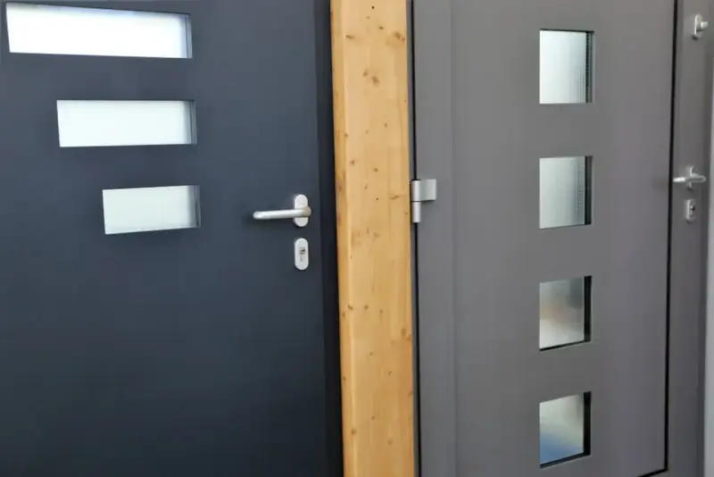 Dwie nowoczesne drzwi wejściowe, jedna ciemnoszara z prostokątnymi przeszkleniami, druga szara z kwadratowymi. Dowiedz się, jak uszczelnić drzwi wejściowe.